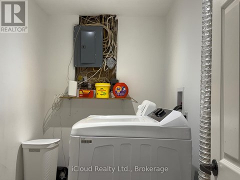A small white washing machine sits in a room with a wall-mounted dryer and a white trash can.