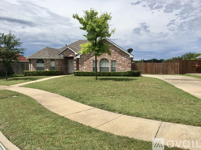 A house with a brown brick exterior and a white door is surrounded by a green lawn and a wooden fence.