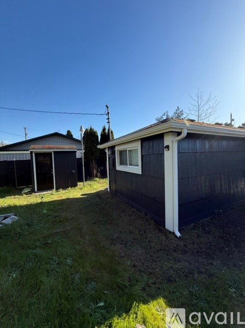 A small house with a white door and a black roof is surrounded by a grassy area.