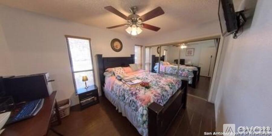 A bedroom with a bed, a desk, and a ceiling fan.