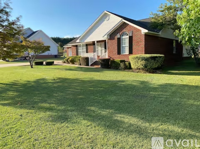 A house with a red brick exterior and a white trim is surrounded by a well-manicured lawn.