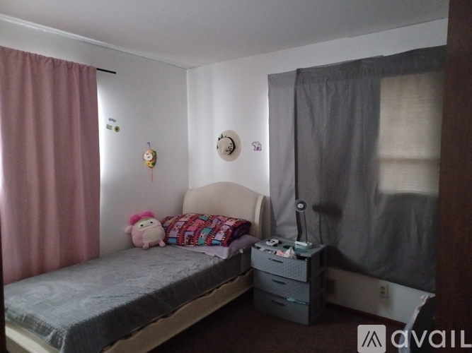 A small bedroom with a bed, a nightstand, and a window with curtains.