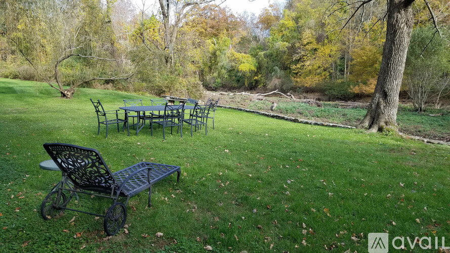 A black metal bench sits in a grassy area with a table and chairs in the background.