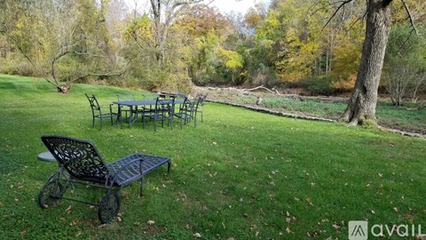 A black metal bench sits in a grassy area with a table and chairs in the background.