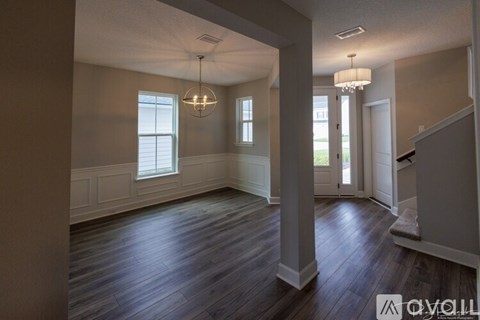 A spacious room with wooden floors and a chandelier hanging from the ceiling.