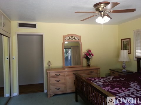 A bedroom with a bed, dresser, mirror, and ceiling fan.