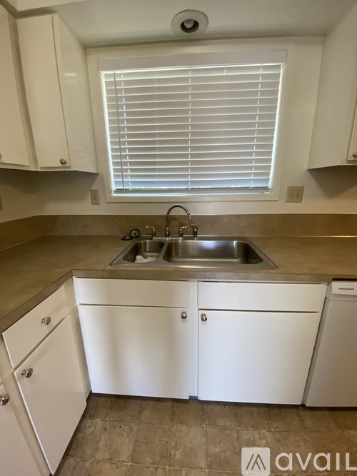A kitchen with white cabinets and a window with blinds.