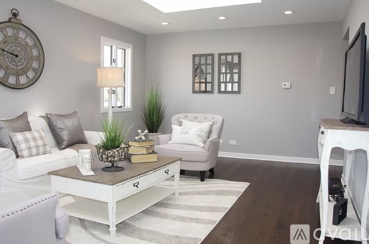 A living room with a white couch, a coffee table, and a large clock on the wall.