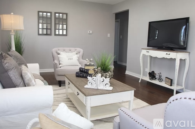 A living room with a white couch, a coffee table with a plant and a camera on it, and a television on a stand.