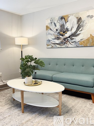 A living room with a green couch, a white coffee table, and a painting on the wall.