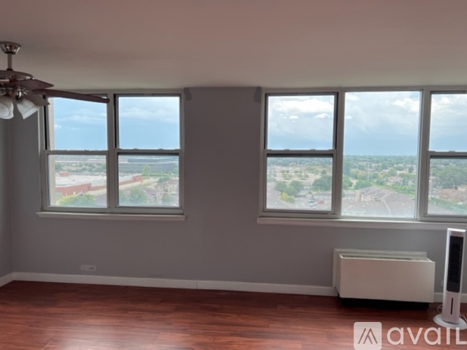 A room with a fan, two windows and a radiator.