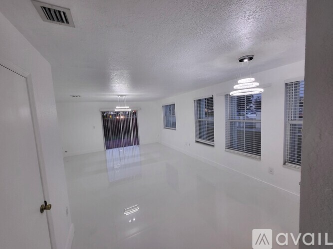 A spacious room with white walls and floor, featuring a ceiling light fixture and a window with blinds.