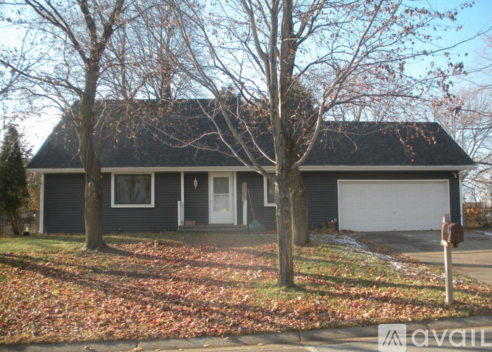 A house with a grey roof and a white door is surrounded by trees and fallen leaves.