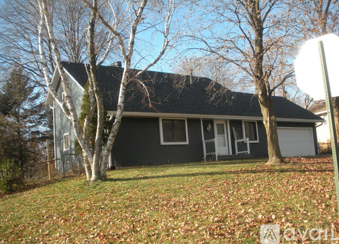 A house with a grey roof and white door is surrounded by trees and grass.