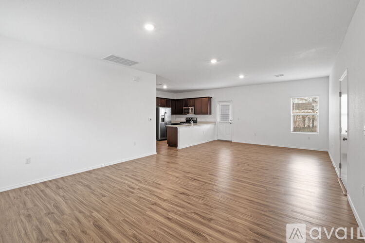 A spacious room with wooden flooring and a kitchen area in the background.