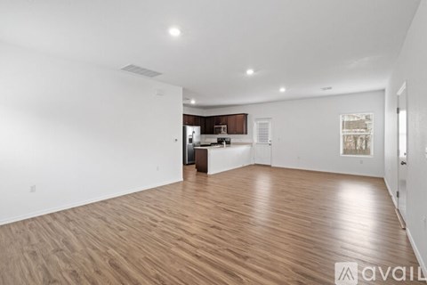 A spacious room with wooden flooring and a kitchen area in the background.