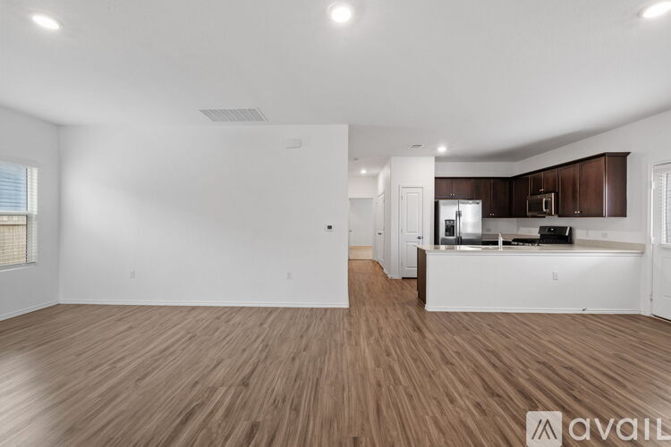 A spacious room with wooden flooring and a kitchen area in the background.