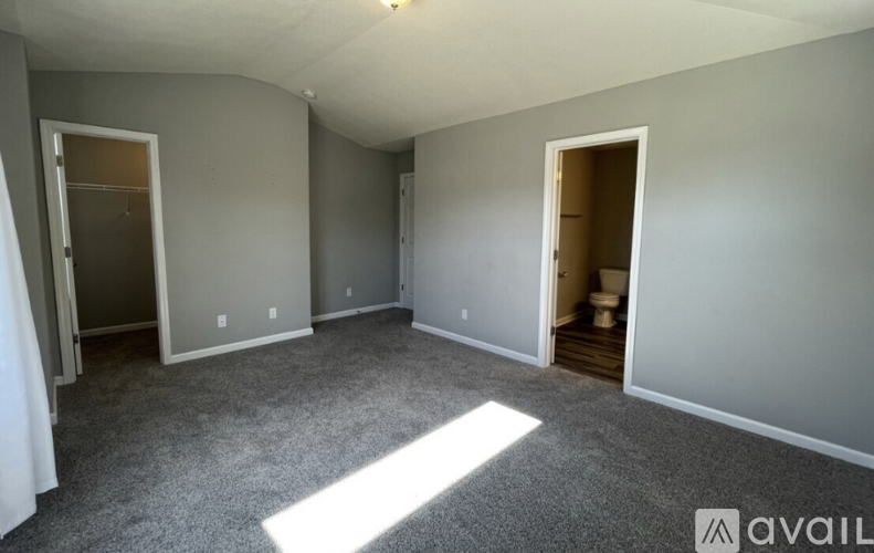 A spacious room with grey carpeting and two open doors.