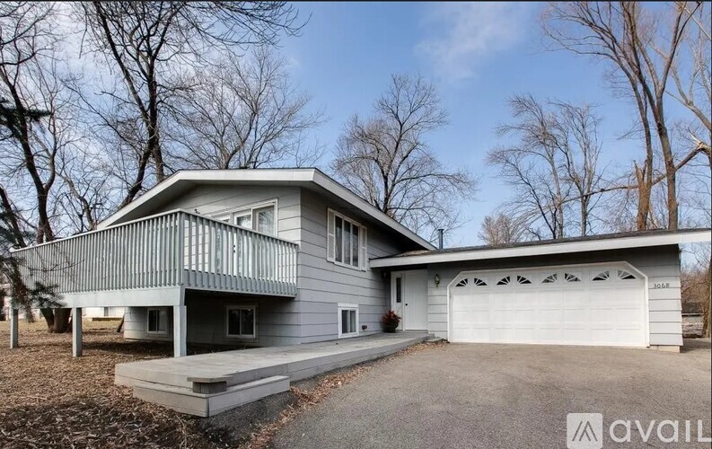 A house with a grey exterior and a white garage door is surrounded by bare trees.