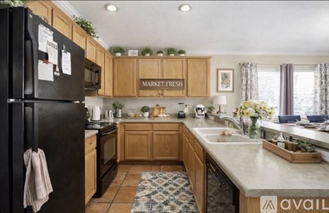 A kitchen with wooden cabinets and a black fridge with a towel hanging on it.