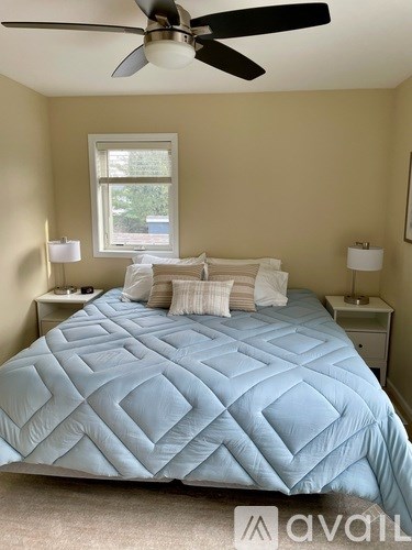 A bedroom with a blue bedspread and two white bedside tables.