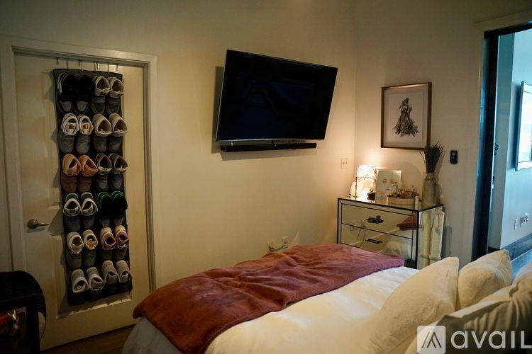 A bedroom with a bed, a TV, a shelf with shoes, and a nightstand with a lamp.