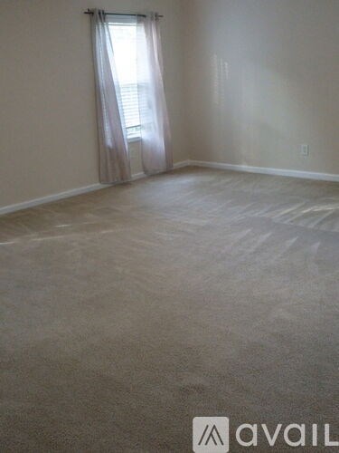 A room with a carpeted floor and a window with curtains.