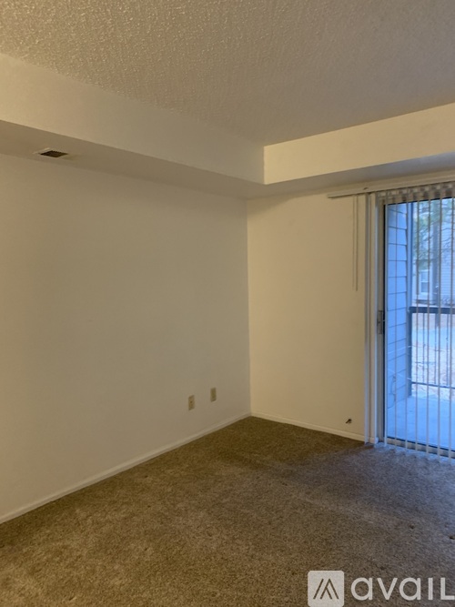 A room with a carpeted floor and a window with a view of a building outside.