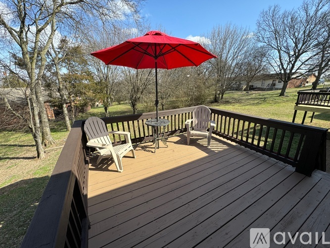 A red umbrella is on a wooden deck with chairs.