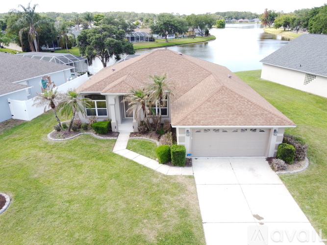 A house with a brown roof is surrounded by a grassy area and a body of water.