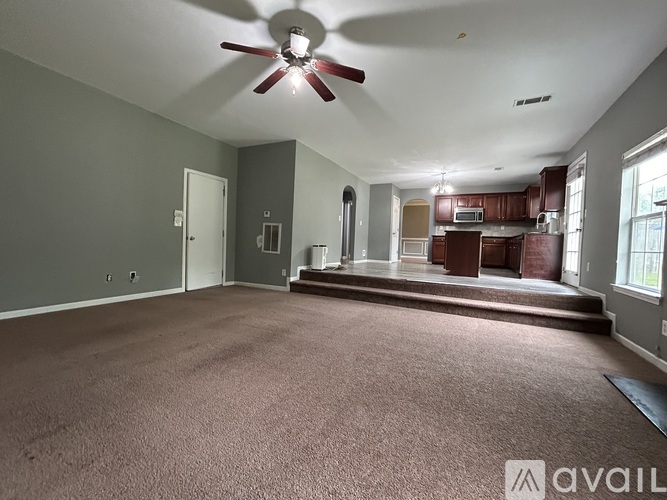 A spacious living room with a ceiling fan and carpeted floor.