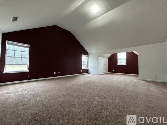 A spacious room with a carpeted floor and two windows.