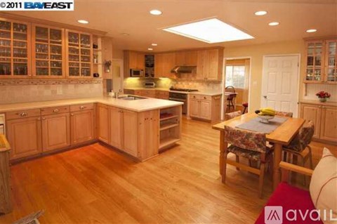 A kitchen with wooden floors and cabinets, a table with chairs, and a window with blinds.