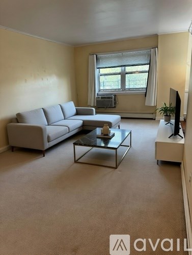 A living room with a grey sofa, a glass coffee table, and a television on a white stand.