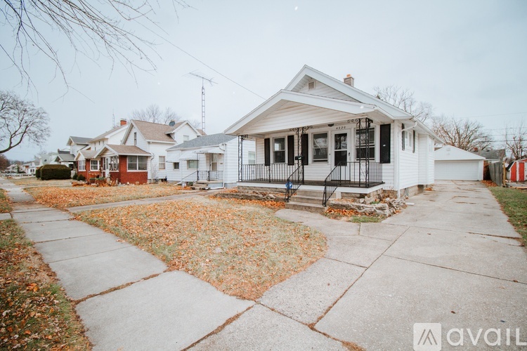 A white house with a black fence and a red car parked in front.