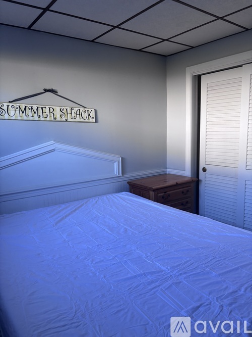 A bedroom with a bed, nightstand, and a sign that says "Summer Shack".