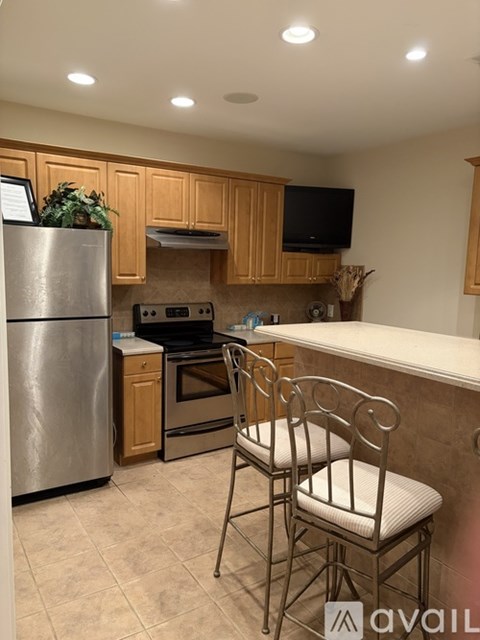 A kitchen with a stainless steel refrigerator, oven, and a bar area with chairs.