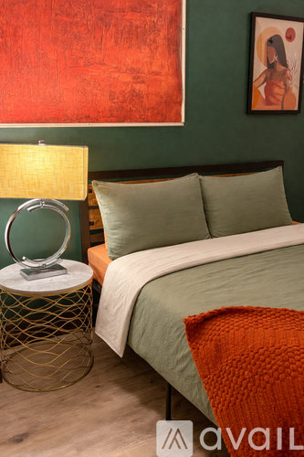 A bedroom with a bed, a side table with a lamp, and a painting on the wall.