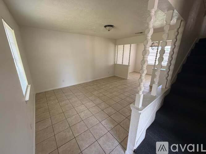 A spacious room with tiled flooring and a staircase with white railings.