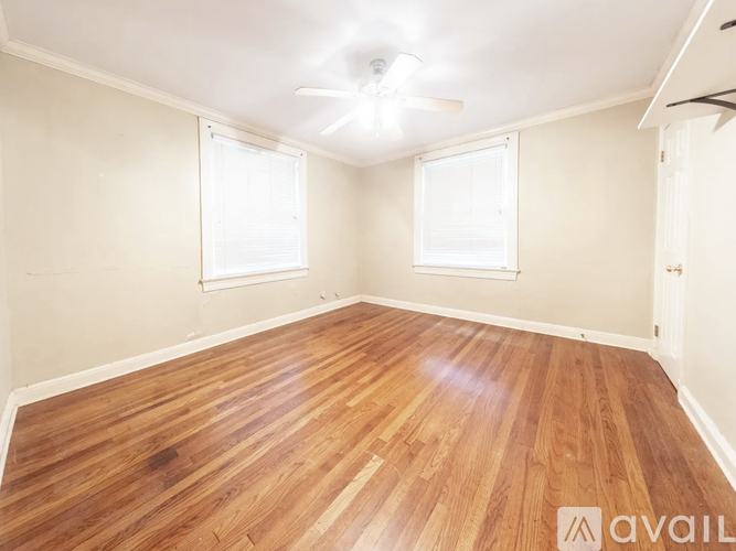 A room with wooden flooring and two windows.
