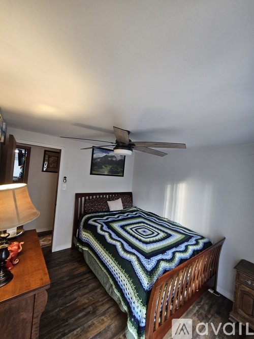 A bedroom with a bed, a ceiling fan, and a lamp on a nightstand.
