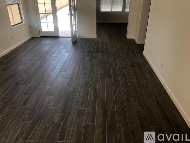 A room with dark wood flooring and a door leading to another room.