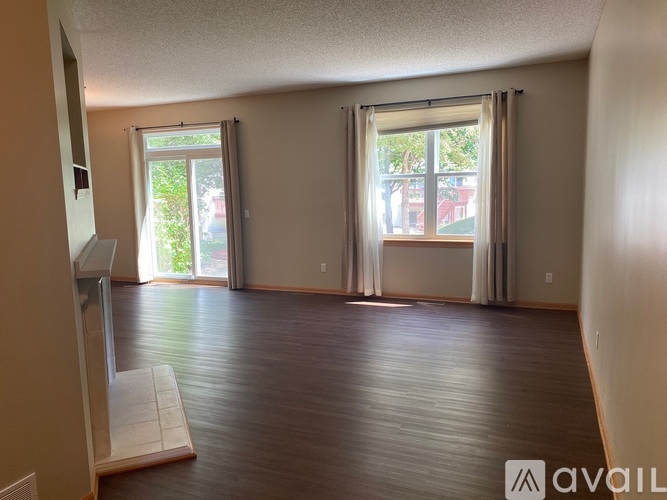 A room with wooden floors and two windows with curtains.