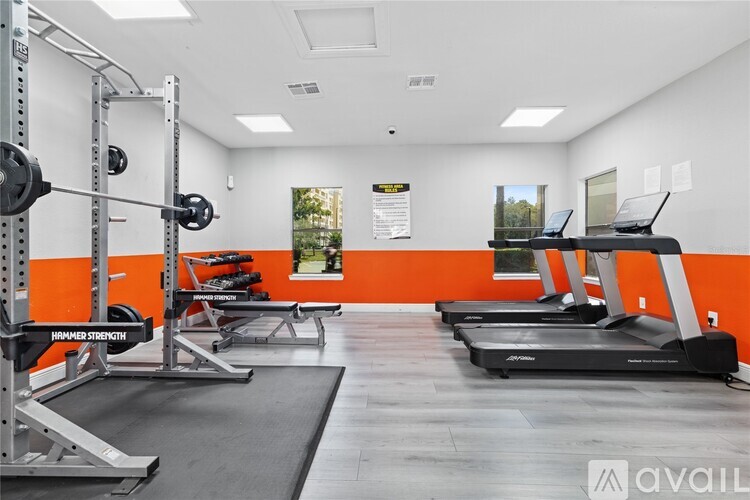 A gym with orange walls and a variety of equipment including treadmills and weightlifting racks.