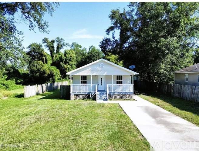 A small white house with a porch and a fence in front of it.
