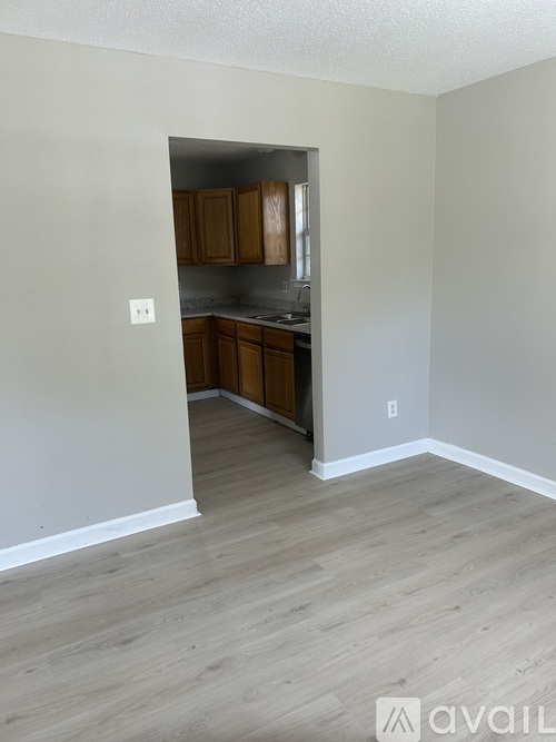 A room with a kitchen area in the background and a hallway leading to it.