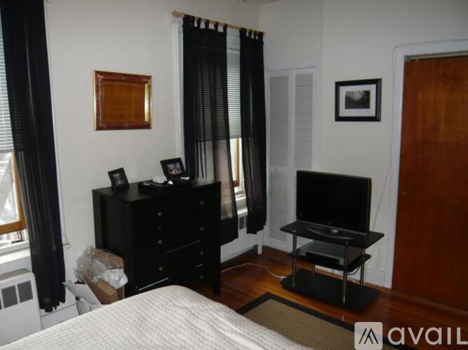 A bedroom with a bed, a TV stand, and a window with black curtains.