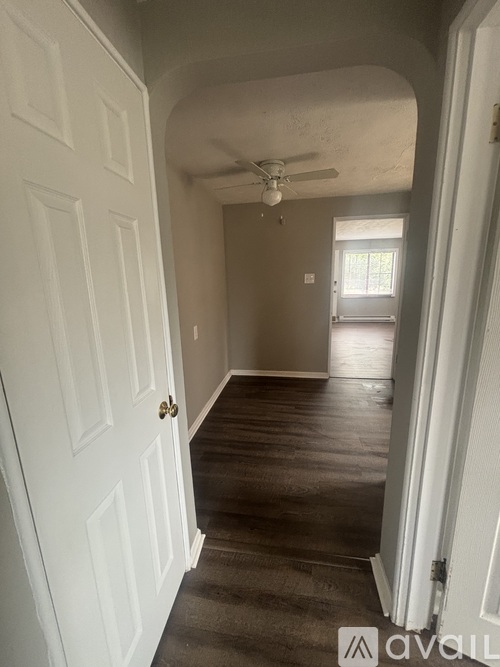 A hallway with a white door and a fan on the ceiling.