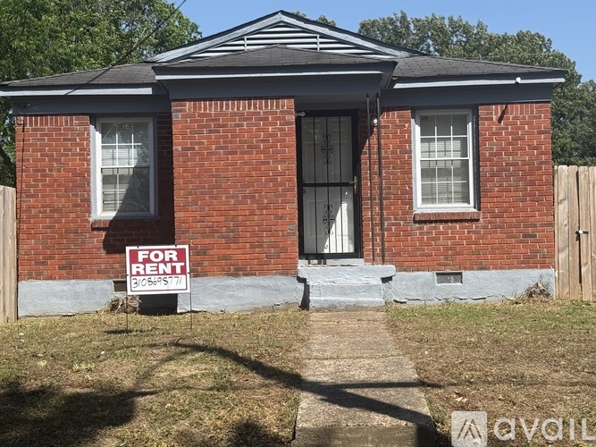 A red brick house with a black door and a "For Rent" sign in front.