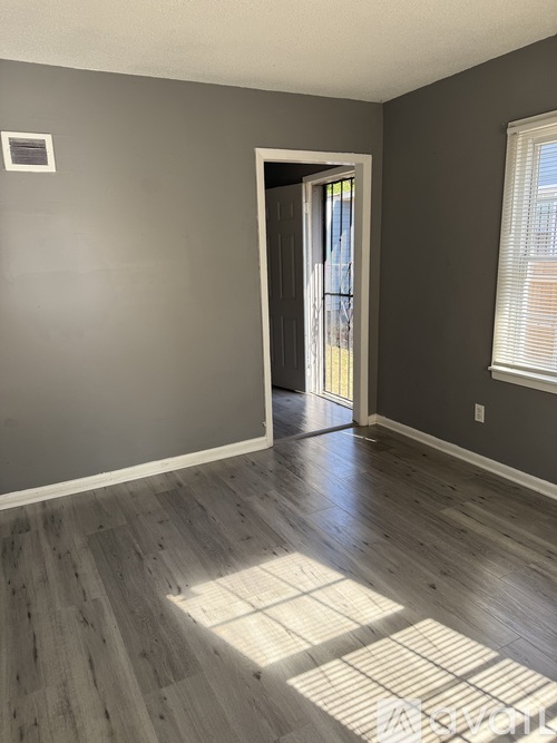 A room with a wooden floor and a doorway leading to another room.